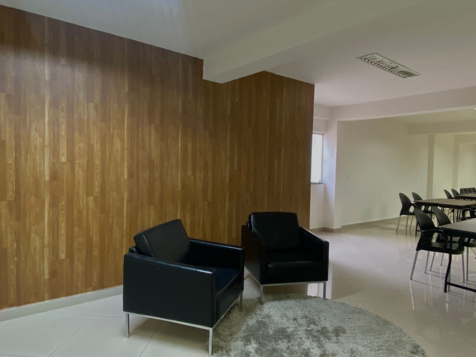 A modern room with a wooden accent wall, a black sofa, and a dining area with chairs and a table.