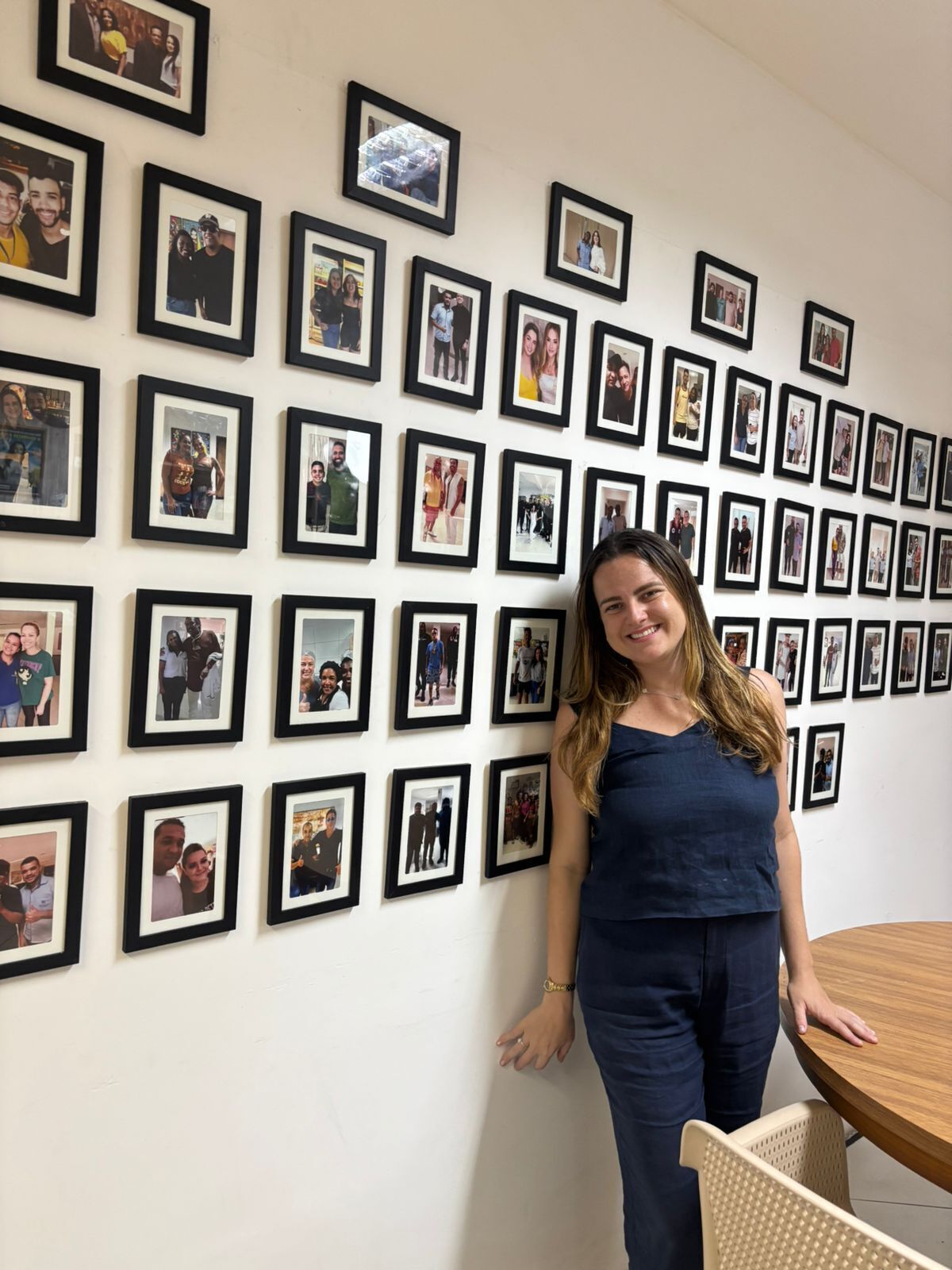 A room with a wall of framed photographs, a round wooden table, and a single chair.