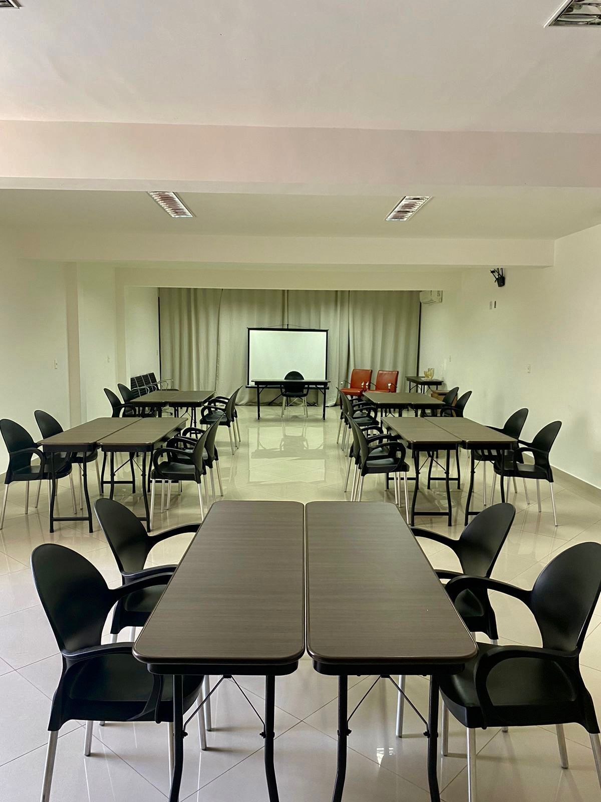 Ein Konferenzraum mit mehreren Tischen und Stühlen, einer Projektionsleinwand und einem Vorhang als Hintergrund.