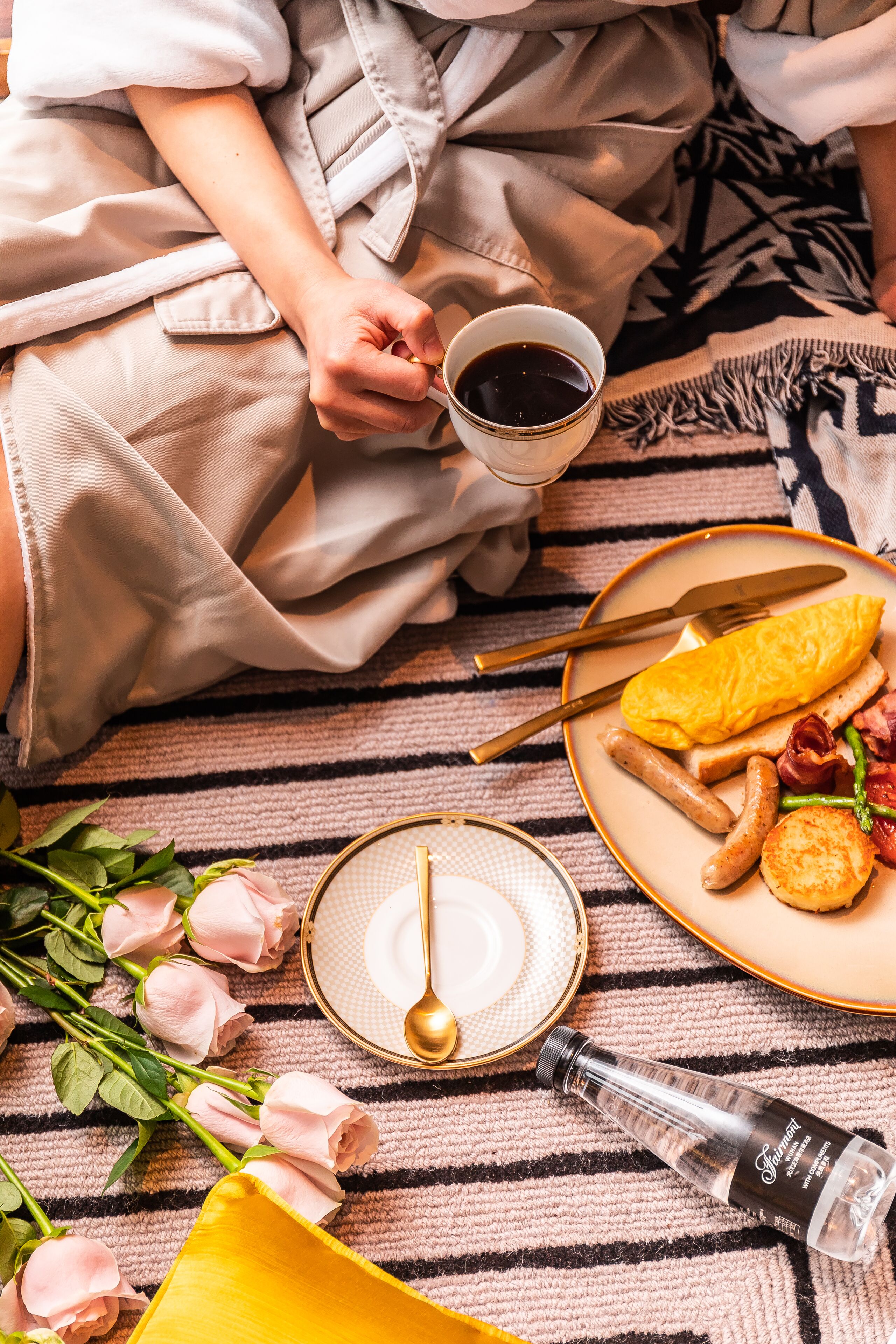 Una escena de desayuno con un plato de comida, una taza de café y una botella de agua sobre una manta a rayas.