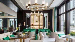 Un hall d’hôtel moderne doté d’un espace salon central, d’un lustre et de grandes fenêtres.