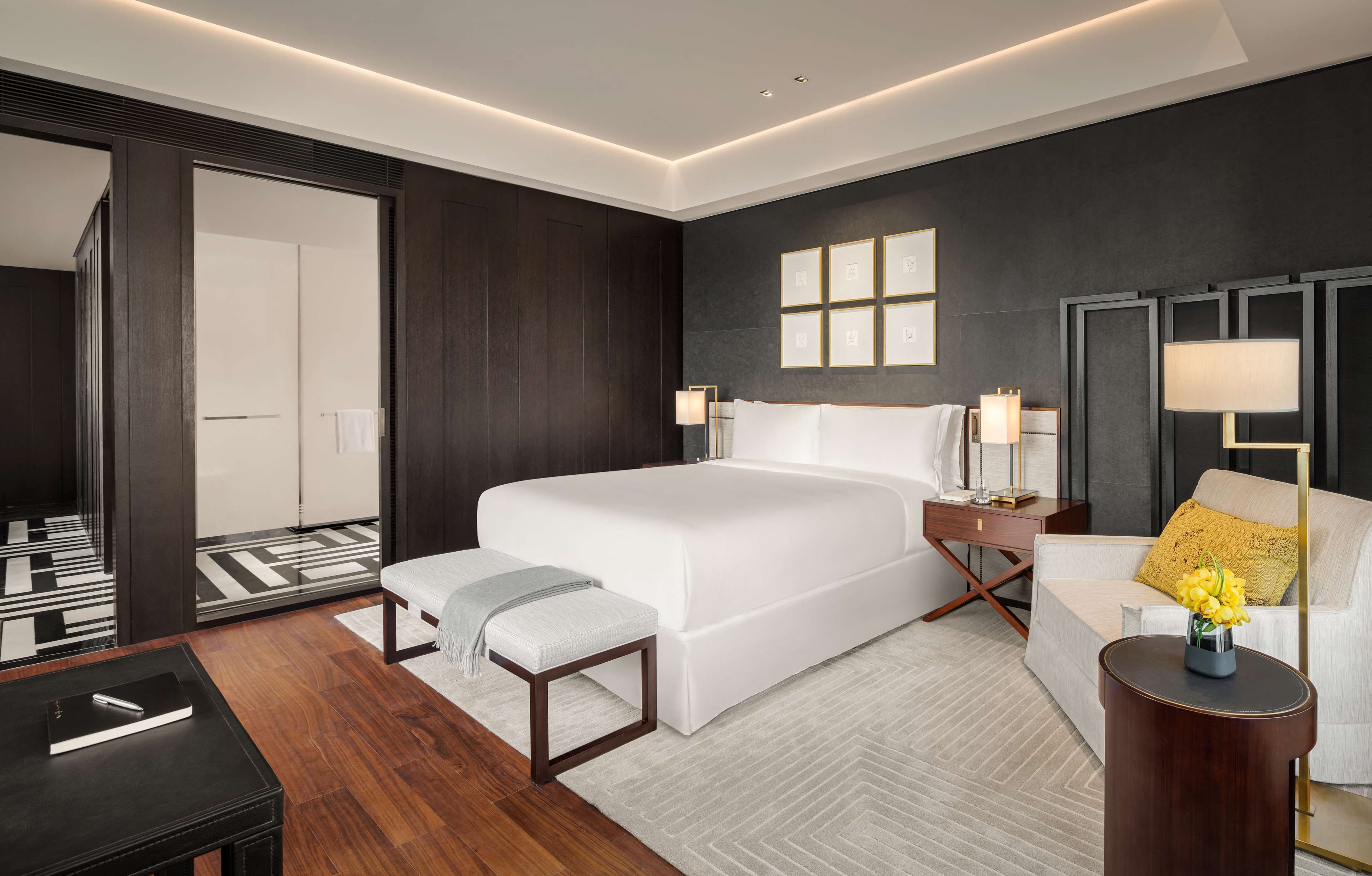 A modern hotel room with a large bed, bedside tables, a sofa, and a small table with a vase of flowers.