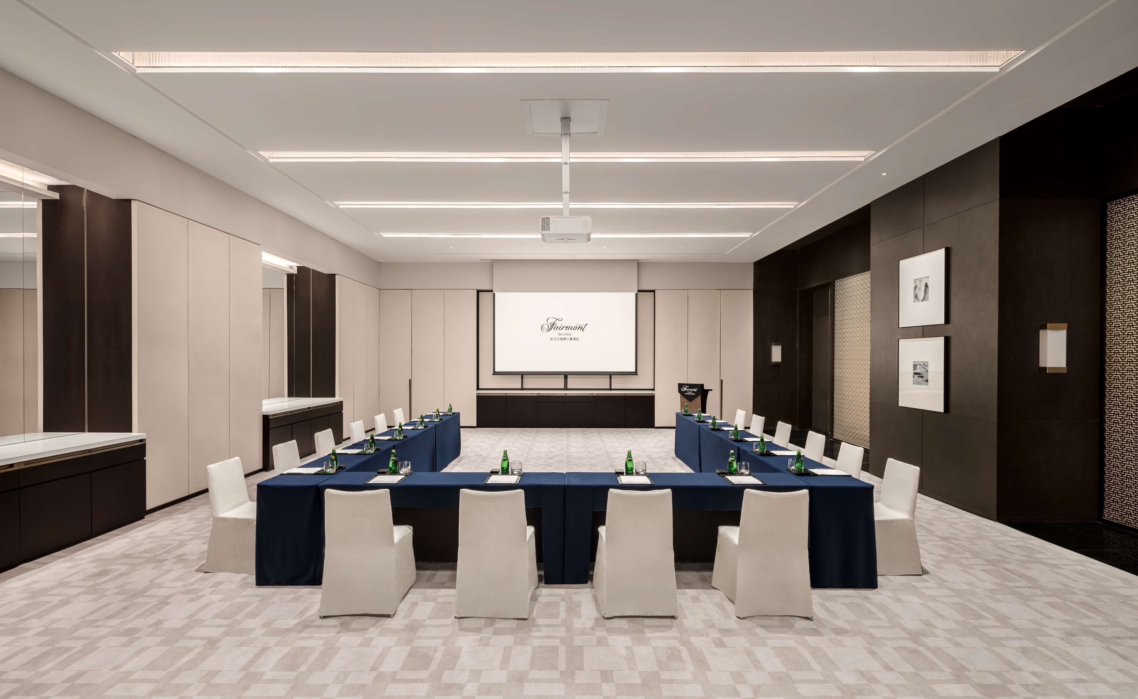 A conference room with a long table, white chairs, a projector screen, and a dark-colored reception desk.