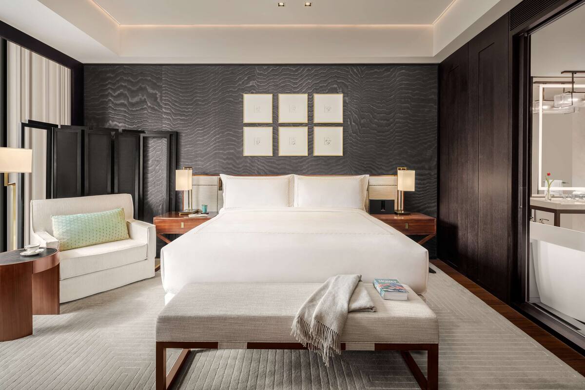 A modern hotel room with a large bed, a sofa, a bedside table, and a nightstand.