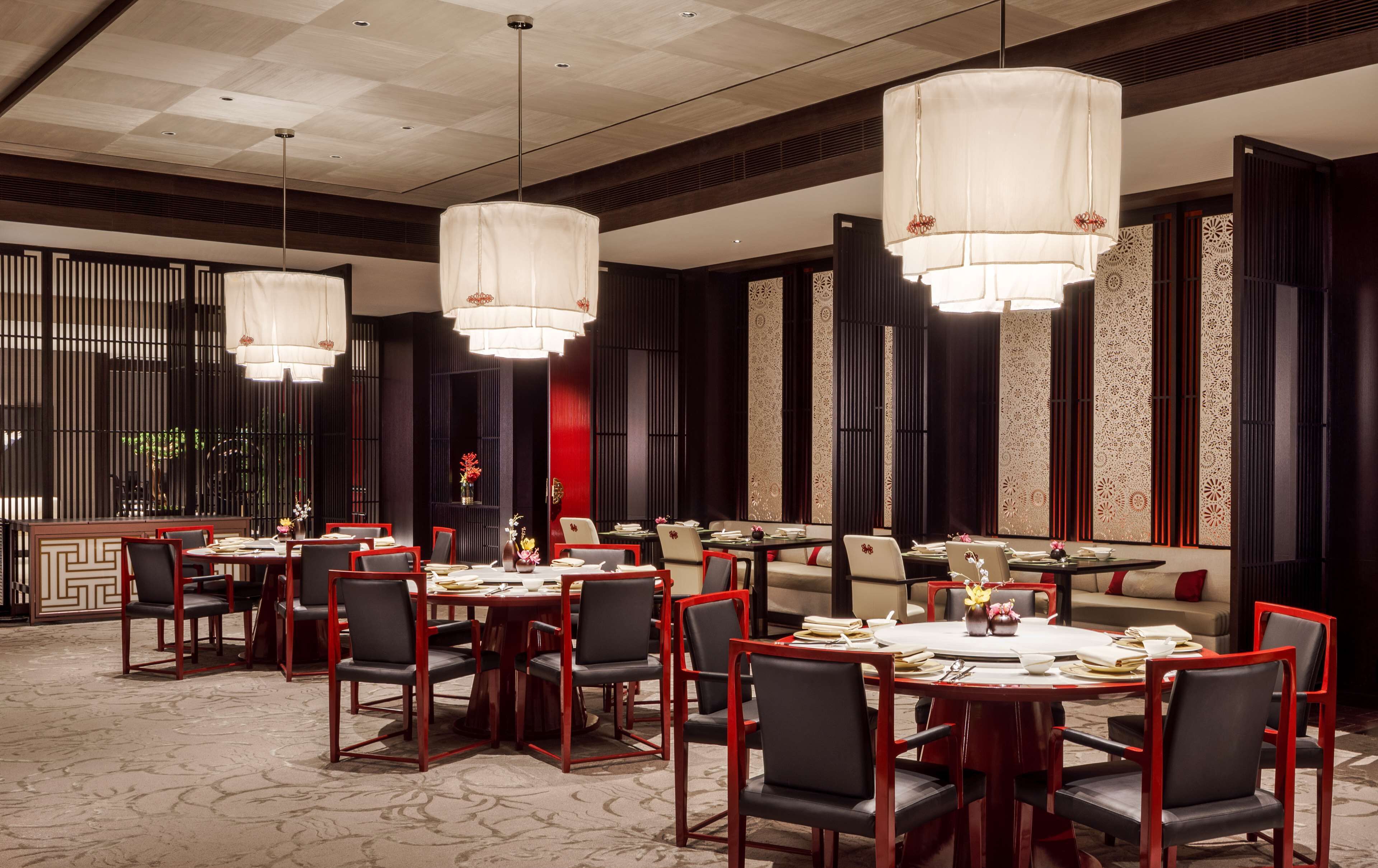 Un espace repas avec des tables et des chaises rondes, de grandes suspensions et des panneaux décoratifs.