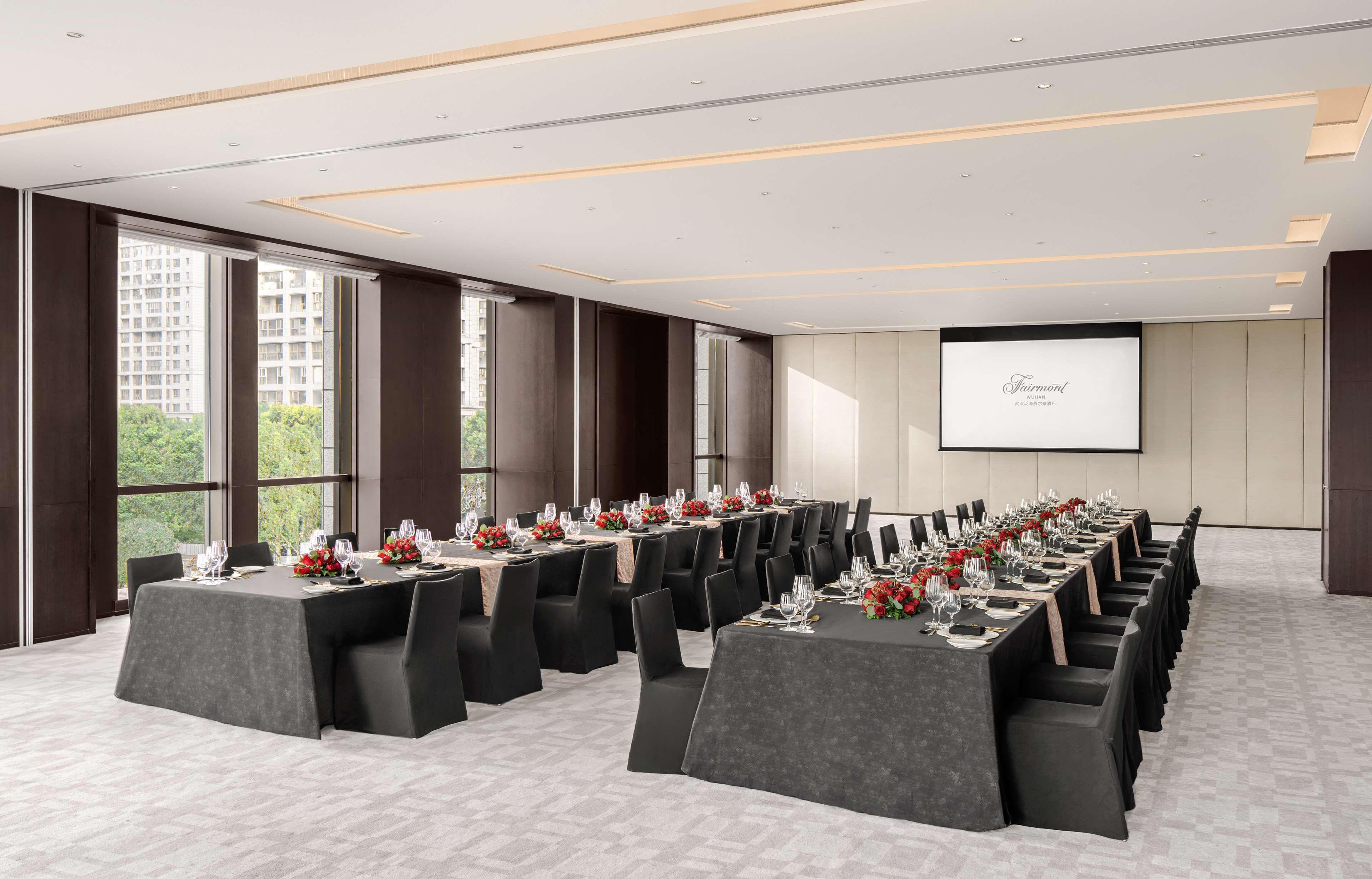 A conference room with long tables, black chairs, and a projector screen displaying the word "Fairmont".