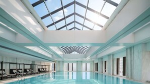 Une grande piscine intérieure dotée d’un toit en verre laissant entrer la lumière du jour, des pièces baignées de soleil grâce à de grandes fenêtres, et un design épuré et moderne.