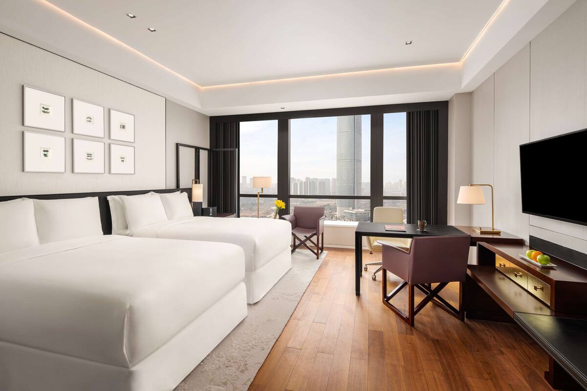 A modern hotel room with two beds, a desk, and a large TV.