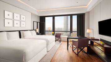 A modern hotel room with two beds, a desk, and a large TV.