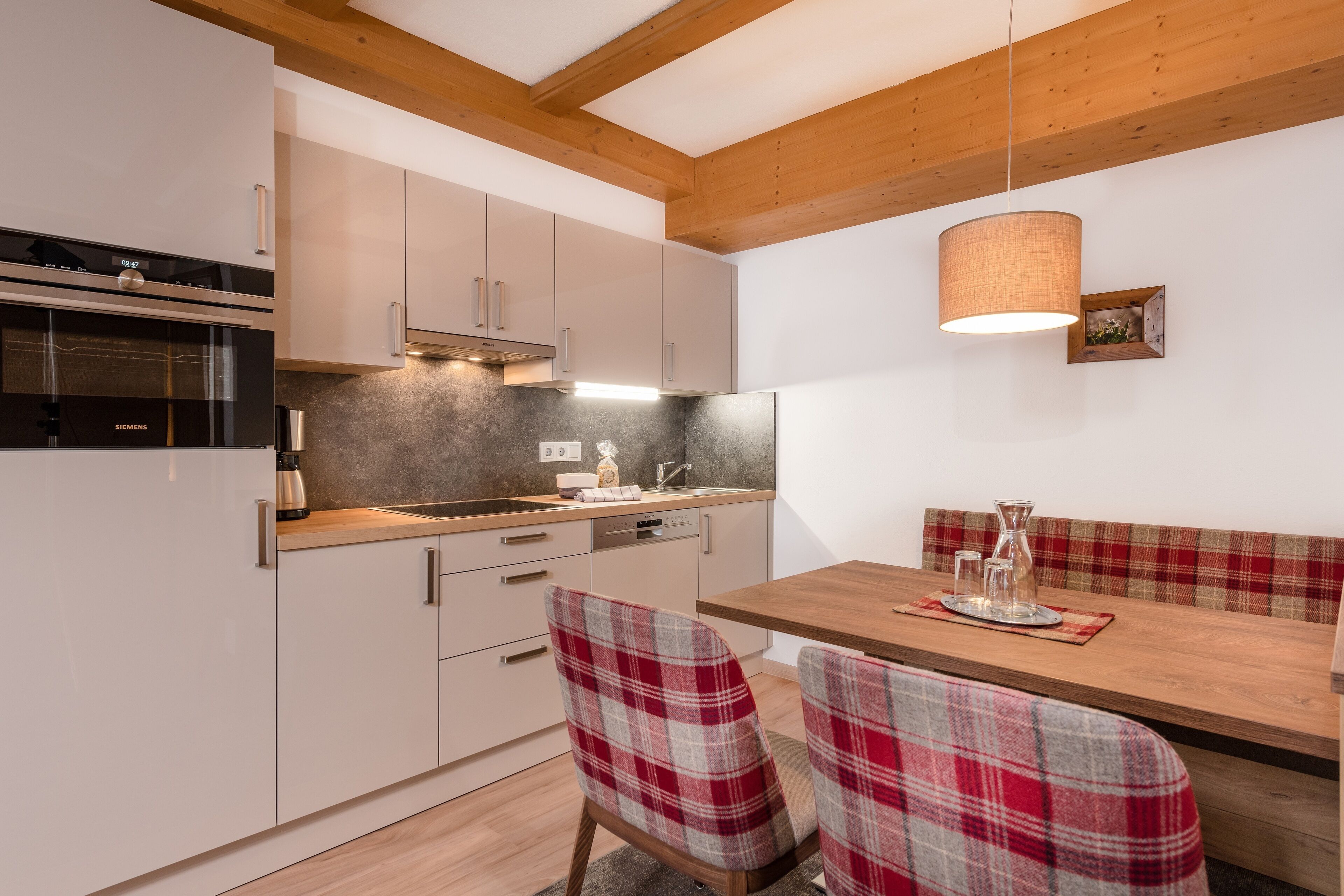 A modern kitchen with white cabinets, a wooden ceiling, and a dining area with plaid chairs and a wooden table.