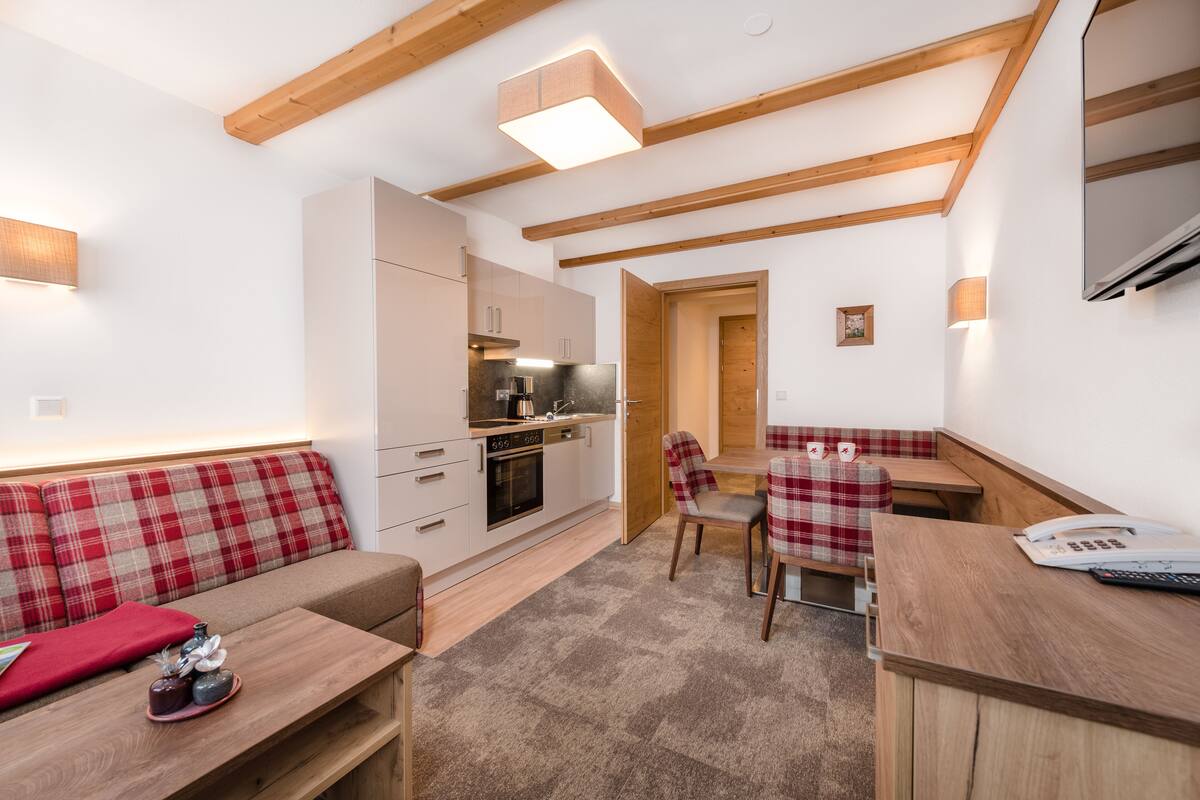 A compact kitchen with modern appliances, a dining area with a wooden table and chairs, and a cozy seating area with a red and white checkered sofa.