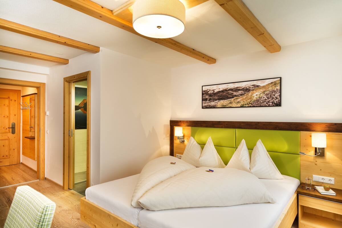A bedroom with a wooden bed frame, a green upholstered headboard, and a wall-mounted picture.