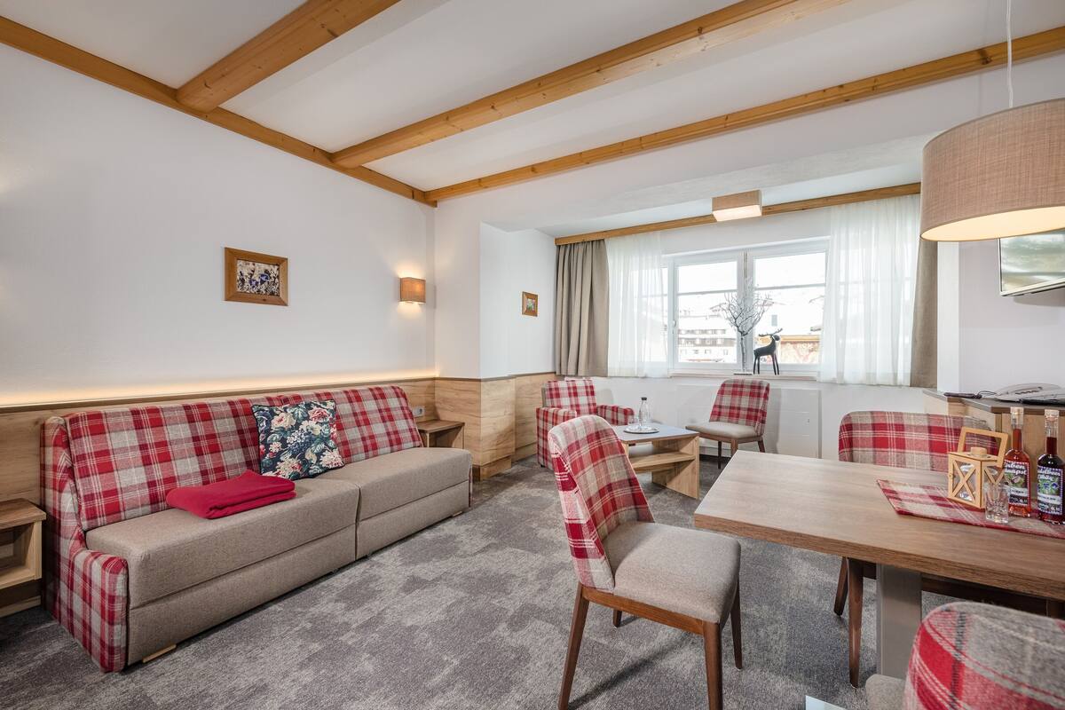 A cozy living area with a sofa, chairs, a wooden dining table, and a window with curtains.
