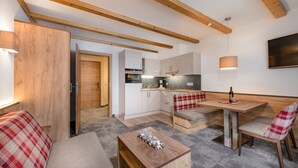 A compact kitchen with wooden beams, a dining area with a bench, and a small table with a decorative item. - Apartments  Garni Alpenrose (Tweng)