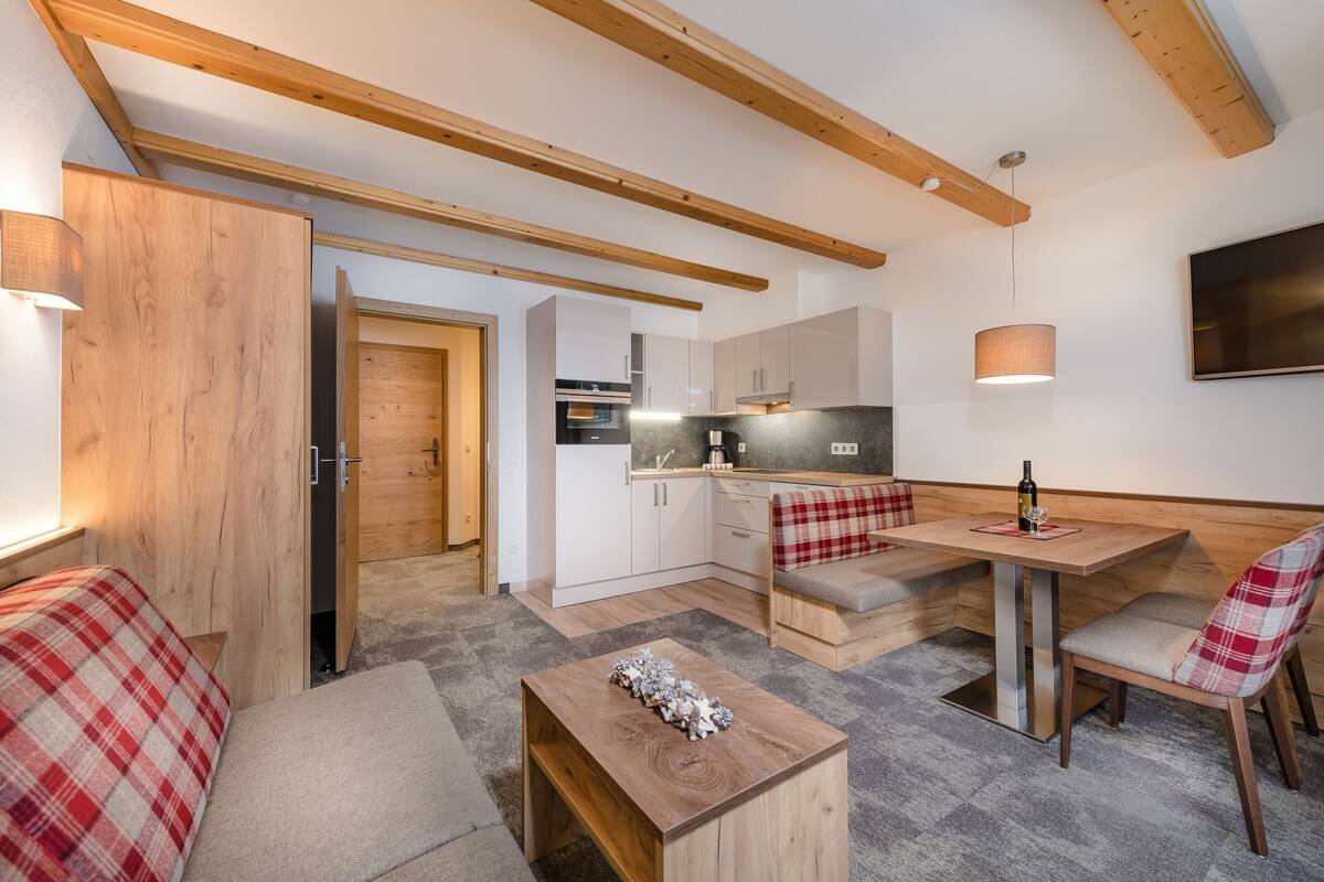 A compact kitchen with wooden beams, a dining area with a bench, and a small table with a decorative item.