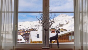 A view through a window of a mountain resort with snow-covered buildings and a clear sky. - Apartments  Garni Alpenrose (Tweng)