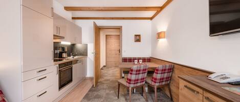 A compact kitchen with modern appliances, a dining area with plaid chairs, and a wooden ceiling.