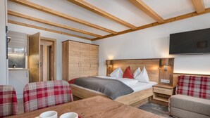 A cozy room with a bed, a TV, a wooden ceiling, and a table with cups. - Apartments  Garni Alpenrose (Tweng)