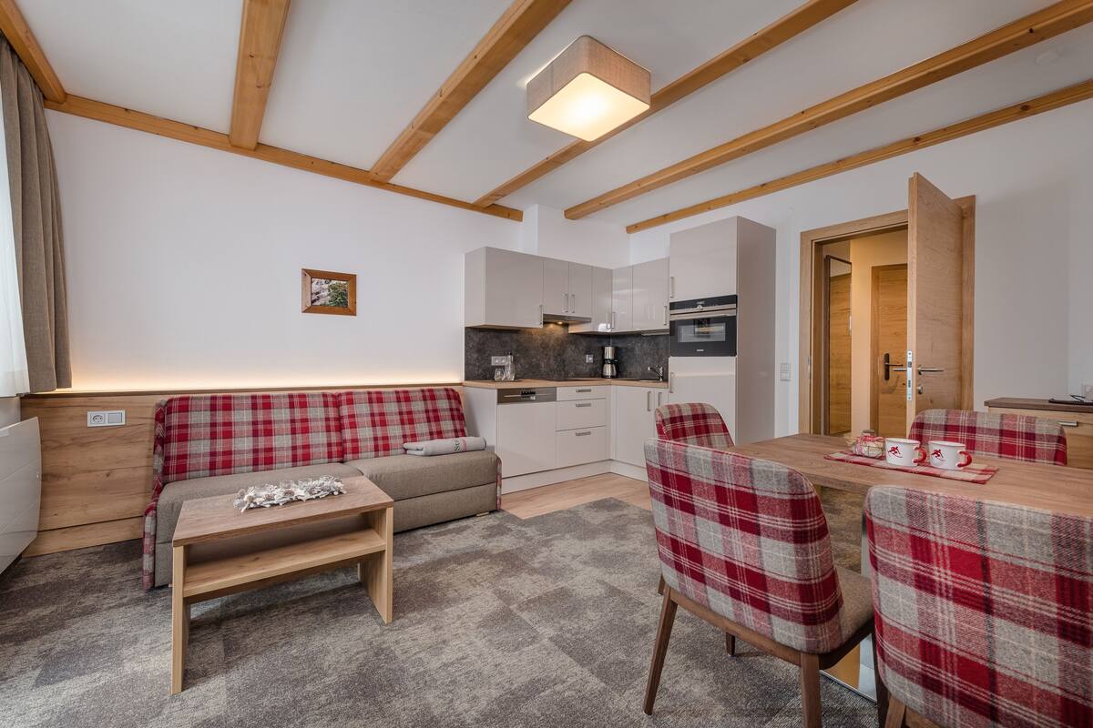A cozy room with a sofa, a dining table with chairs, a kitchen area, and a wooden ceiling.
