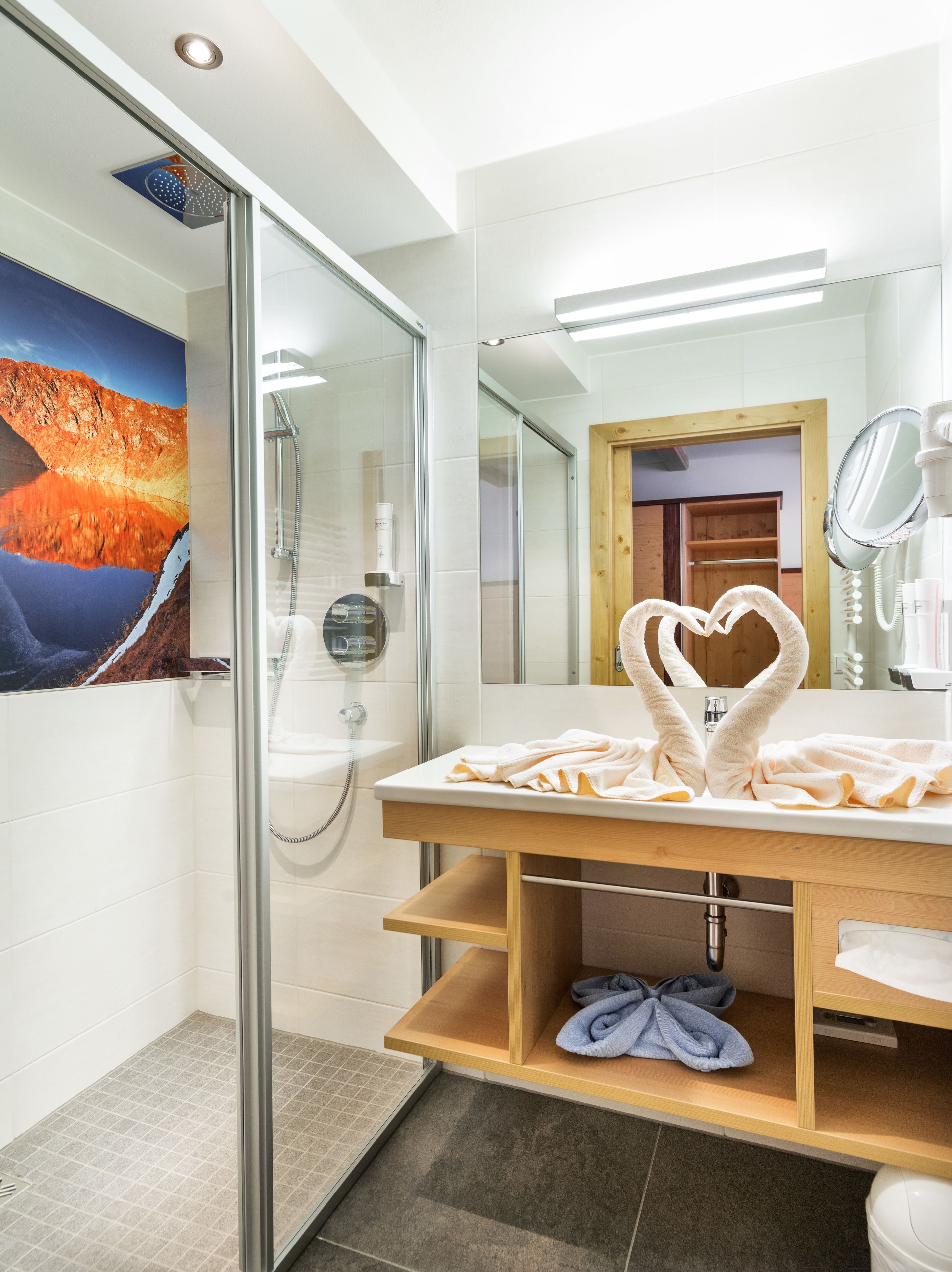 Un baño moderno con ducha envuelta en vidrio, tocador con toalla en forma de corazón y un espejo grande.