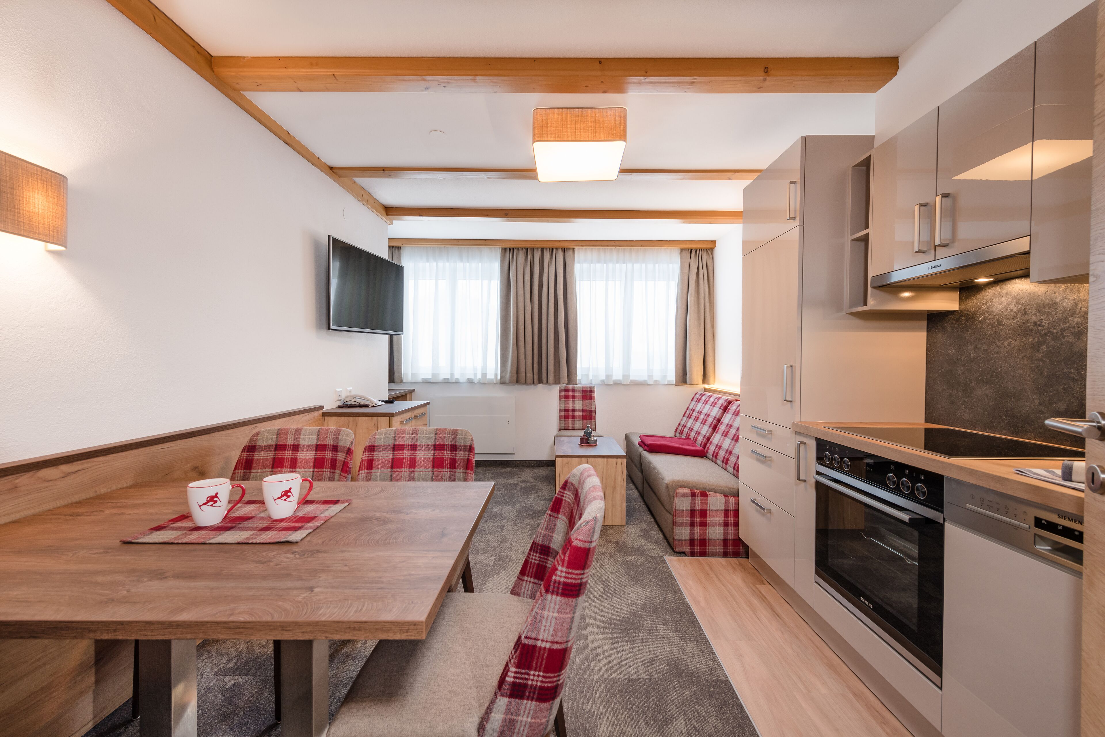 Una cocina moderna con horno empotrado y microondas, un comedor con mesa de madera y sillas a cuadros, y una zona de estar acogedora con sofá y una mesita auxiliar.