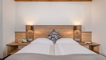 Una cama doble con cabecera de madera, dos mesitas de noche con lámparas y un cojín con estampado floral.