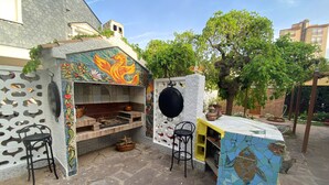 An outdoor kitchen area with a tiled backsplash, a hanging pot rack, and two bar stools.