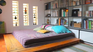 A room with a bed, a bookshelf, and a window with curtains.