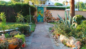 A stone pathway leading to a colorful mosaic gate, surrounded by various plants and rocks.