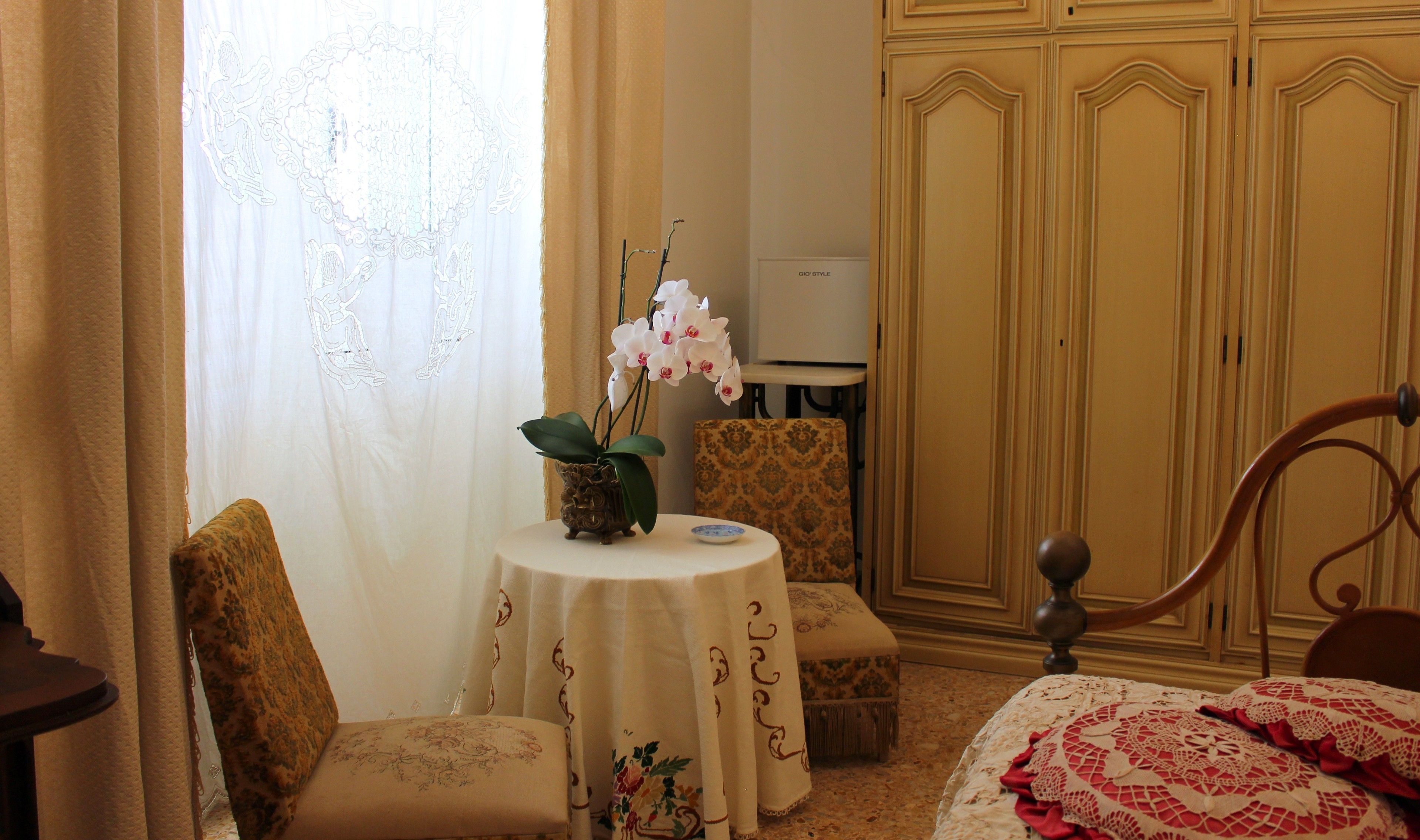 A room with a bed, a chair, a small table with a plant, and a wardrobe.