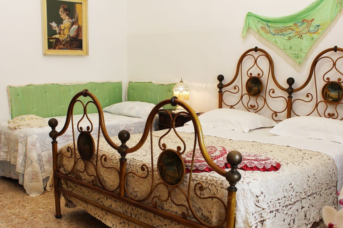 Ein Schlafzimmer mit einem grünen, gepolsterten Kopfteil, einem hölzernen Bettgestell mit aufwendiger Verzierung und einer weißen Bettdecke.