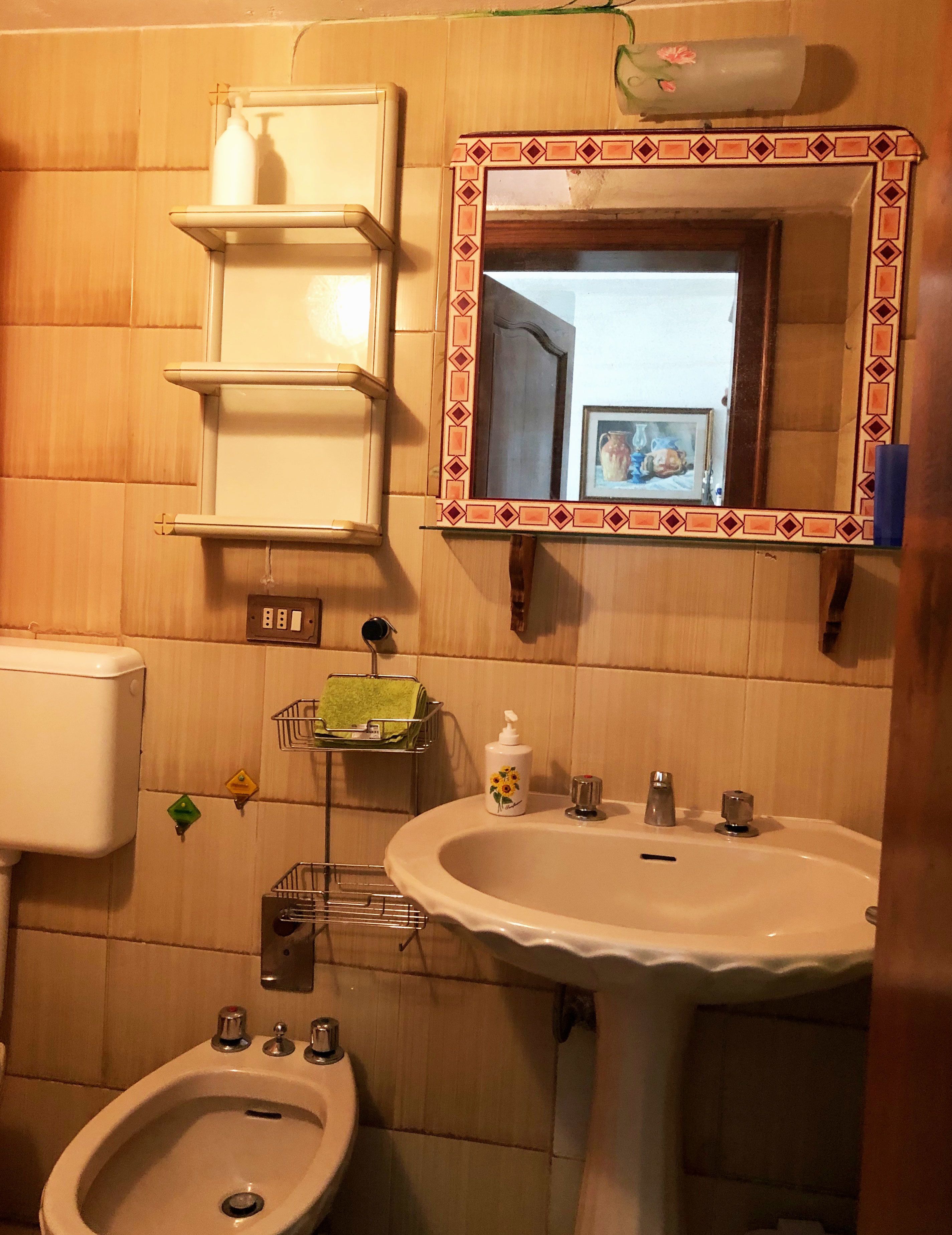 Een badkamer met toilet, bidet, wastafel en spiegel met decoratieve lijst.