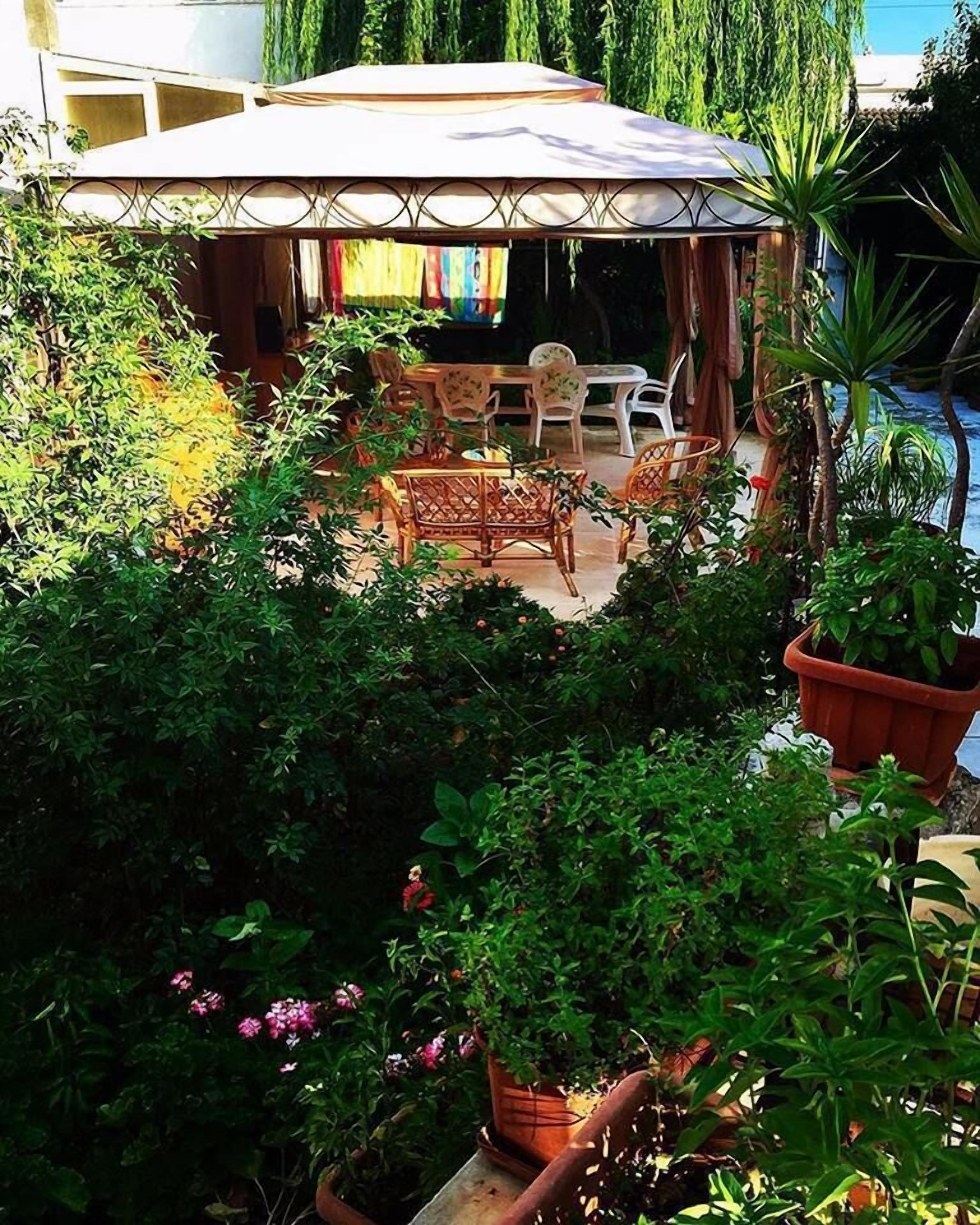 Un espace extérieur aménagé, abrité et doté de mobilier en osier et de plantes en pot.