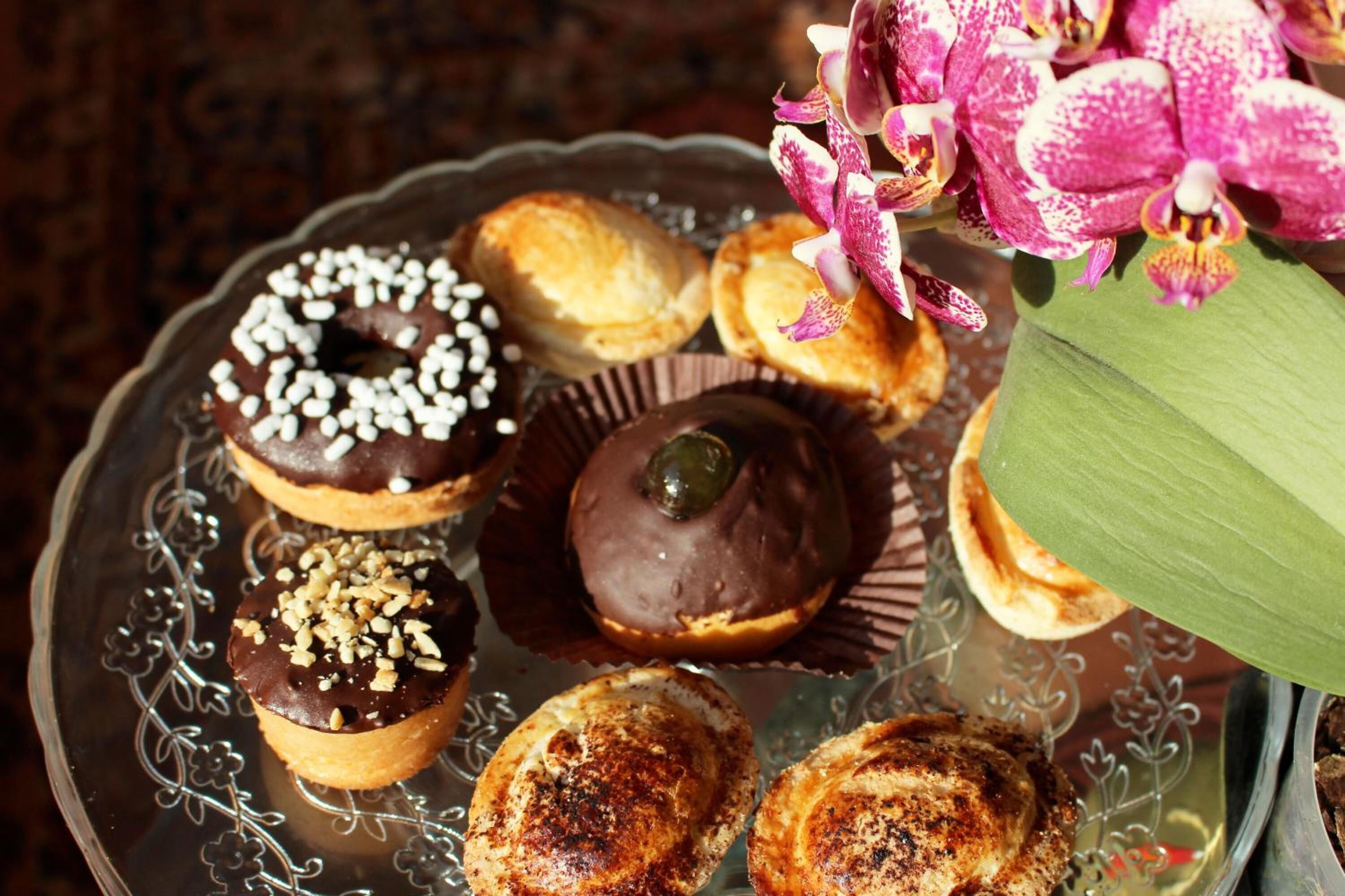 Una variedad de pasteles en un plato de vidrio decorativo, incluyendo rosquillas cubiertas de chocolate y otras delicias dulces.