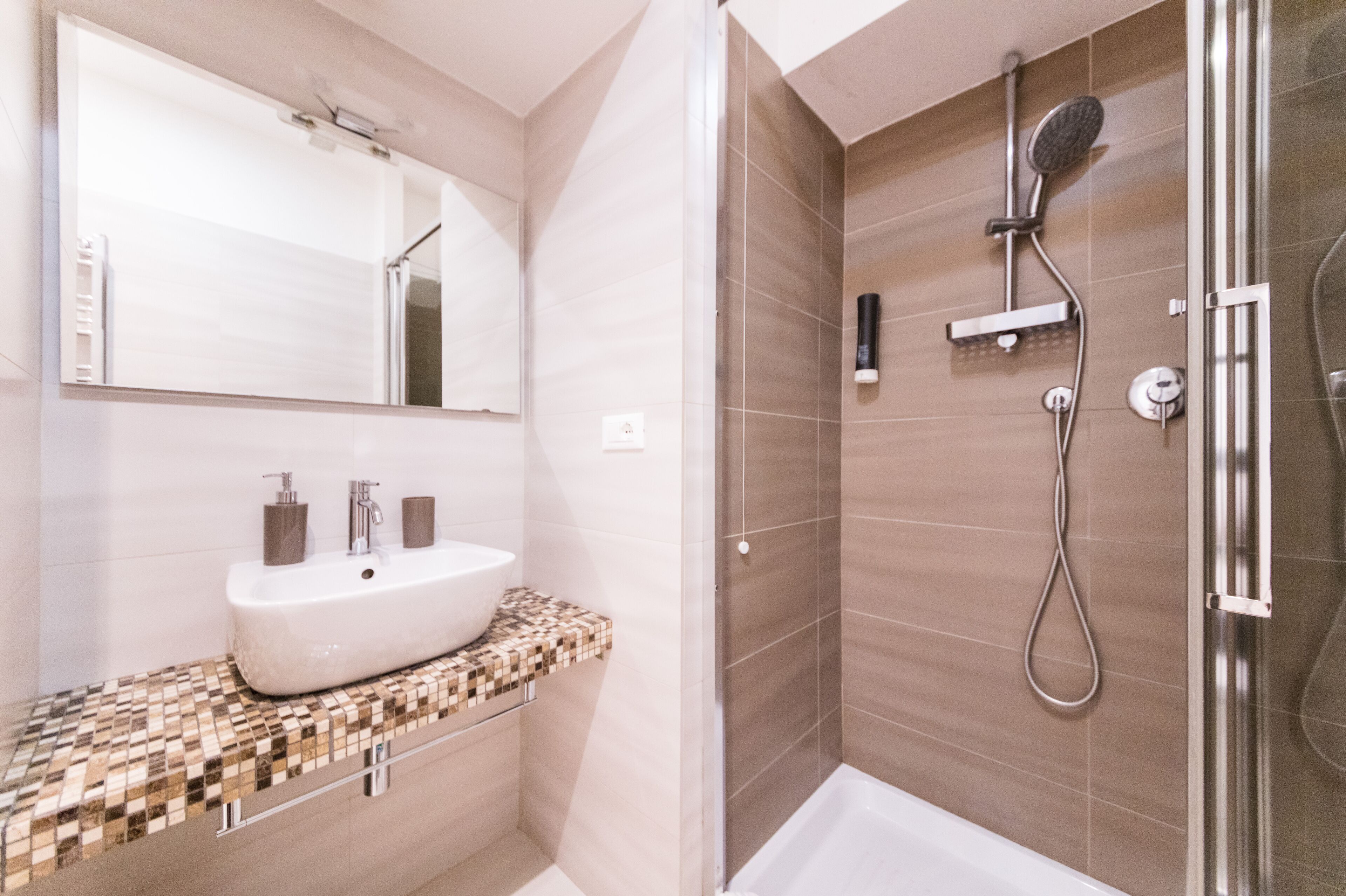 Un bagno moderno con uno specchio grande, un lavabo con due rubinetti, una doccia con soffione a mano e box doccia in vetro.