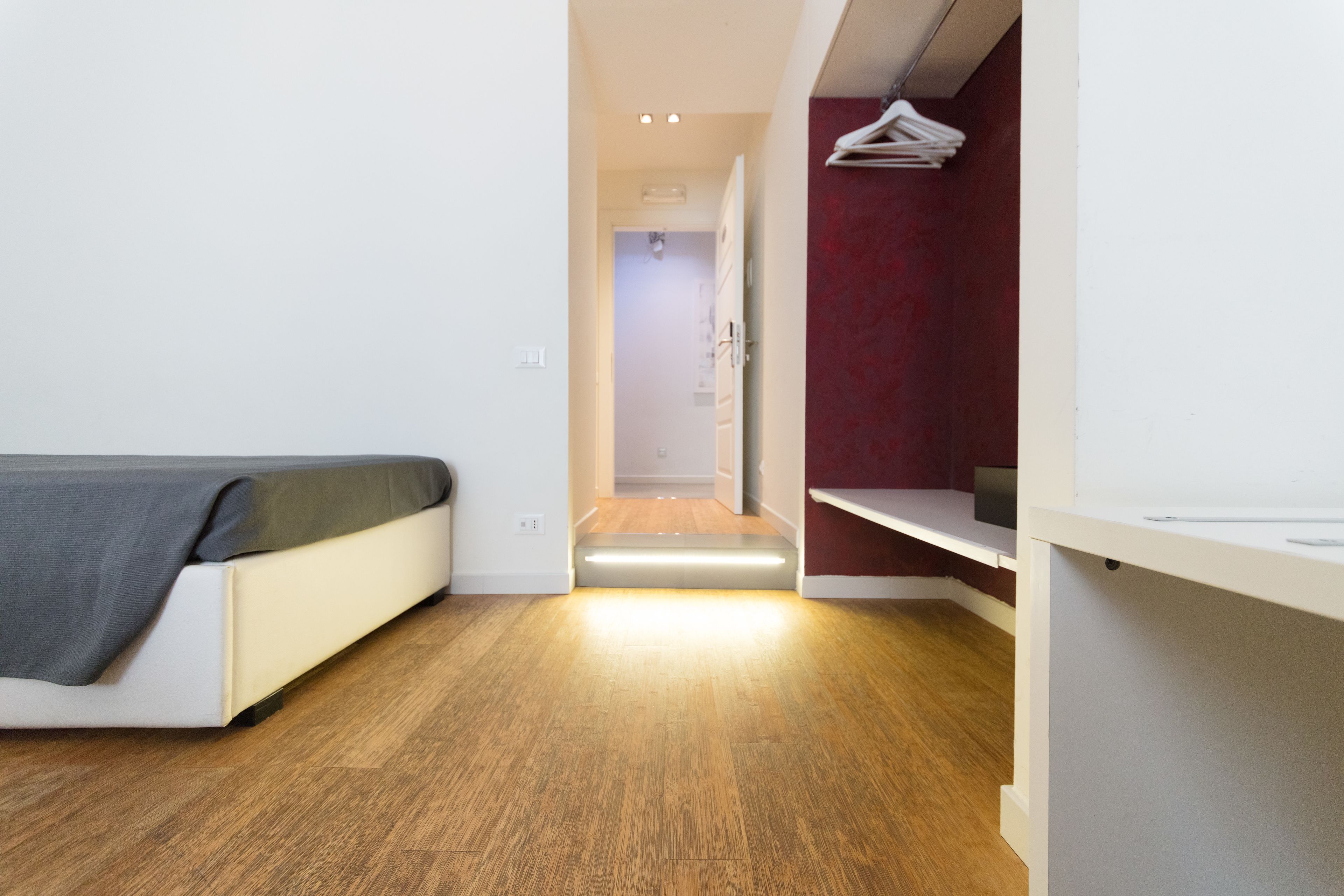 Une chambre moderne avec un lit, un plancher en bois, un mur d’accent rouge et une armoire blanche.