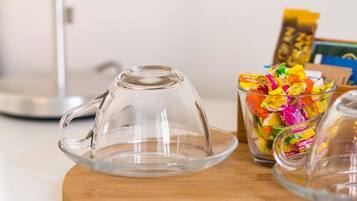 A clear glass coffee pot on a wooden surface, a glass mug filled with colorful candies, and a blurred background.