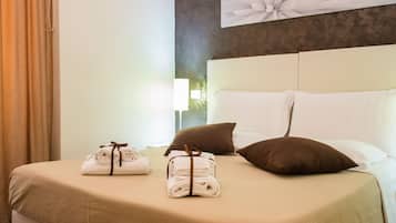 A neatly made bed with a beige bedspread, two brown pillows, and two rolled towels tied with brown ribbons.