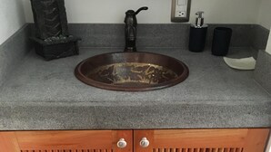 Kylpyhuone, jossa on graniittinen työtaso, puinen allaskaappi ja koristeellinen kivi.