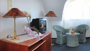A bedroom with a bed, two chairs, a small table, a TV, and a lamp. - Hotel Mühlbergblick (Frankenblick)