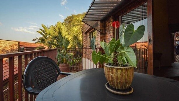 A patio area with a round table and chairs, surrounded by potted plants and a brick wall. - Quail's Nest (Roodepoort)