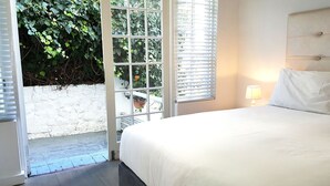 Un dormitorio con cama, mesita de noche, lámpara y vistas a la vegetación por una ventana.