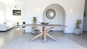 Una sala moderna con una mesa de comedor central, un sofá blanco y plantas en macetas.