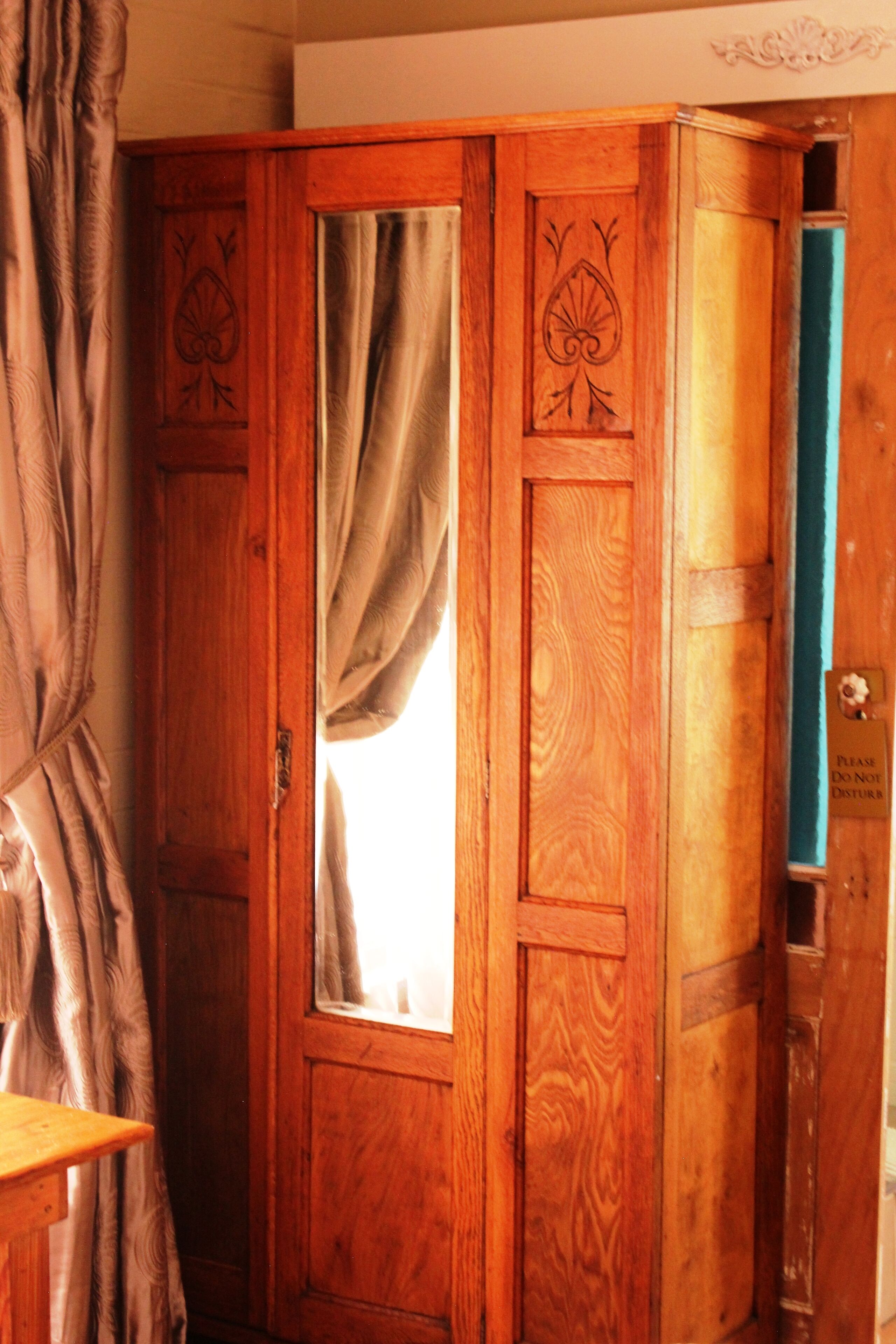 A wooden wardrobe with a mirror and a door with a window.
