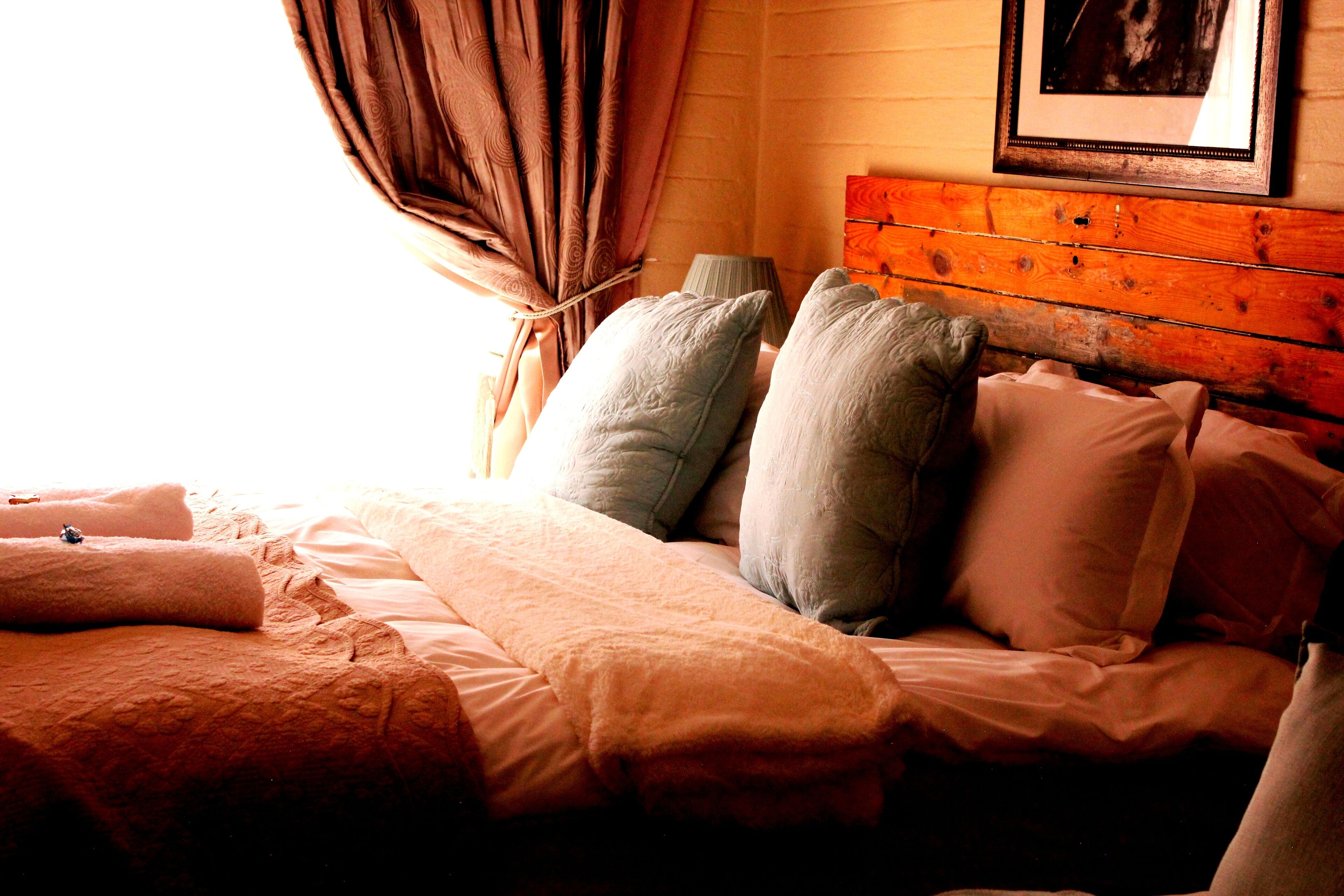 A bed with multiple pillows and a blanket, a wooden headboard, and a framed picture on the wall.