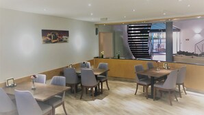 A modern dining area with a long wooden table and several chairs, a counter with a vase of flowers, and a staircase leading to an outdoor area. - A&M Hotel Barsinghausen (Barsinghausen)