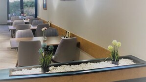 A modern dining area with a long table, multiple chairs, and a decorative plant arrangement. - A&M Hotel Barsinghausen (Barsinghausen)