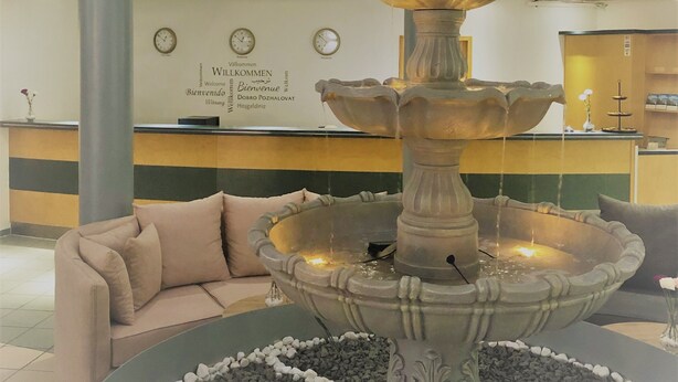 A multi-level lobby with a central fountain, a reception desk, and a staircase. - A&M Hotel Barsinghausen (Barsinghausen)