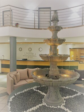 A multi-level lobby with a central fountain, a reception desk, and a staircase. - A&M Hotel Barsinghausen (Barsinghausen)