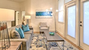 A living room with a sofa, armchair, coffee table, and a painting on the wall.